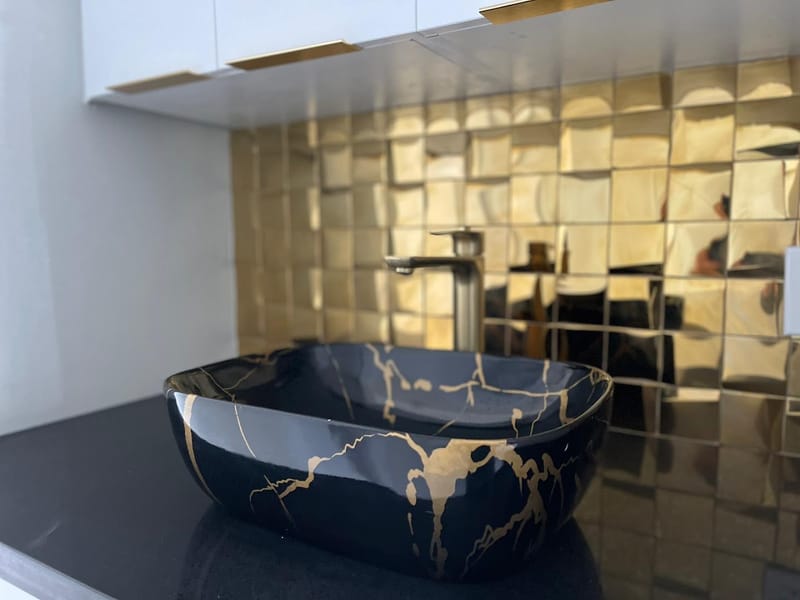 Black and gold vessel sink with brass backsplash